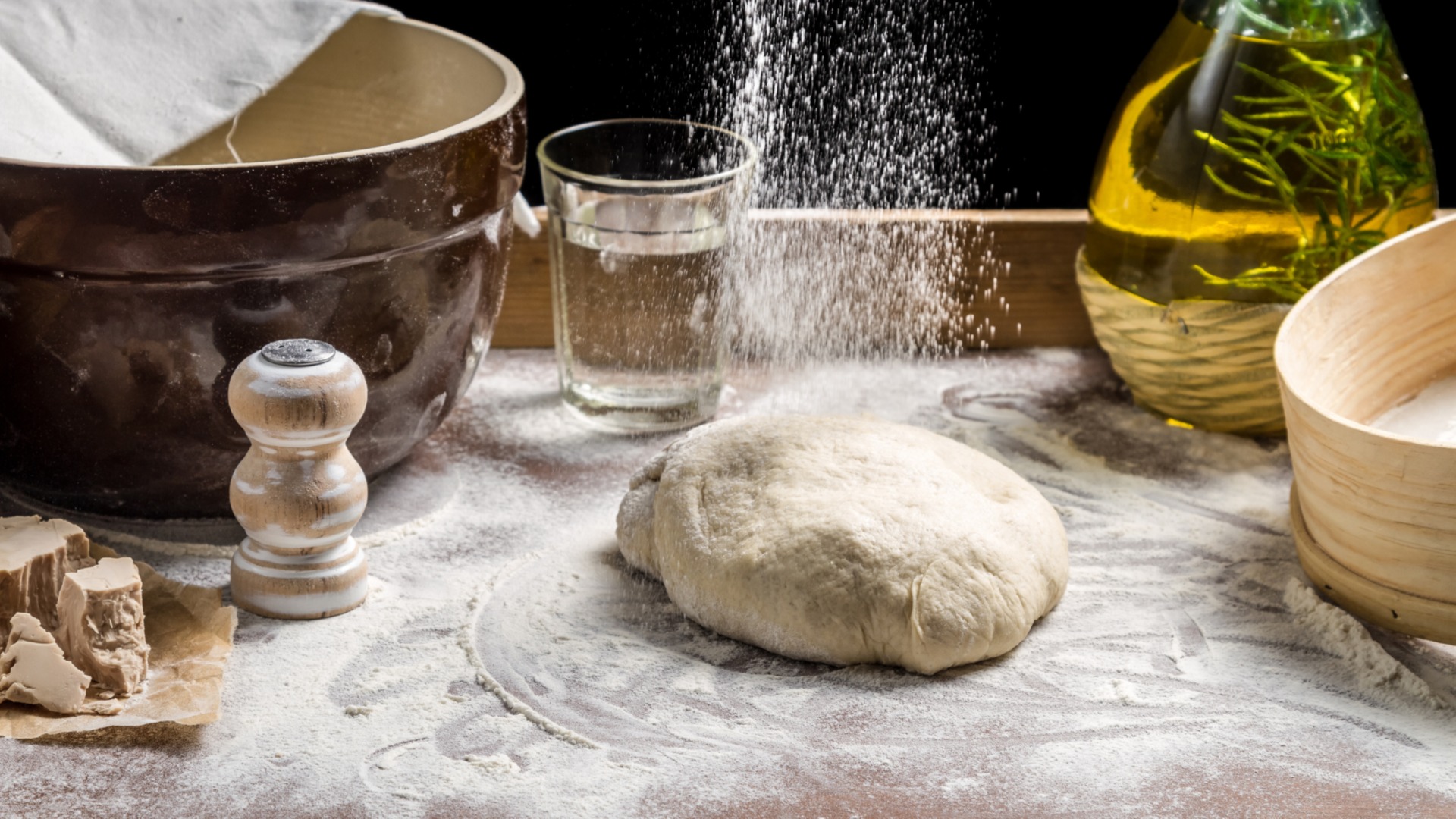 Bread dough being prepared on a floured surface with baking ingredients